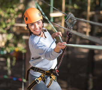 woman with an orange helmet holding onto a rope in adventure park